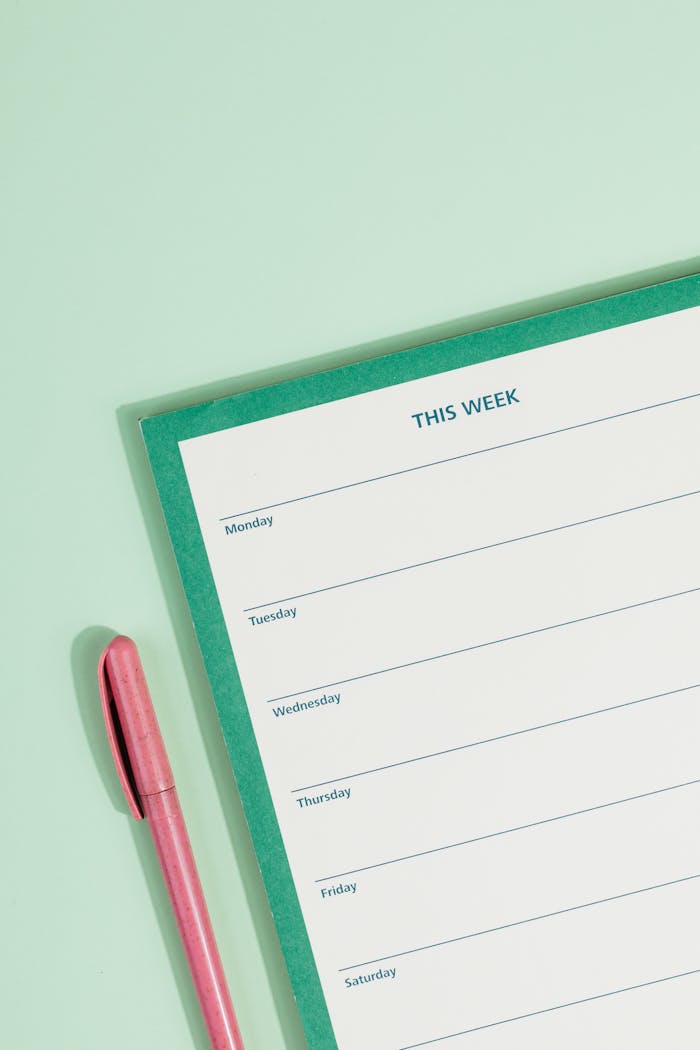 Minimalistic image of a weekly planner with a pink pen on a pastel green background.